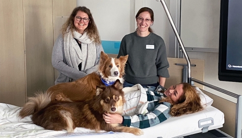 v. l. Linda‐Maria Vietz und Stefanie Birkenbusch mit Nala und Lou (vorne). Im Bett die Kursteilnehmerin Marie‐Louise Ammenhäuser, (Gesundheits‐ und Krankenpflegerin am Krankenhaus in Bad Arolsen) in einer praktischen Übung mit den Hunden.