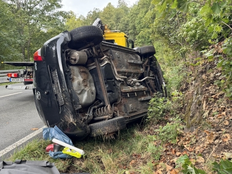 Das beschädigte Fahrzeug nach dem Unfall auf der Landstraße, das auf der Seite liegt. Die Feuerwehr war im Einsatz, um die Fahrerin zu befreien und die Unfallstelle abzusichern.