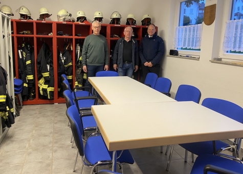 Drei Vertreter der Feuerwehr stehen am 20. Oktober 2026 im Feuerwehrhaus hinter den neu angeschafften Stühlen, die künftig auch den örtlichen Vereinen für Veranstaltungen zur Verfügung stehen.